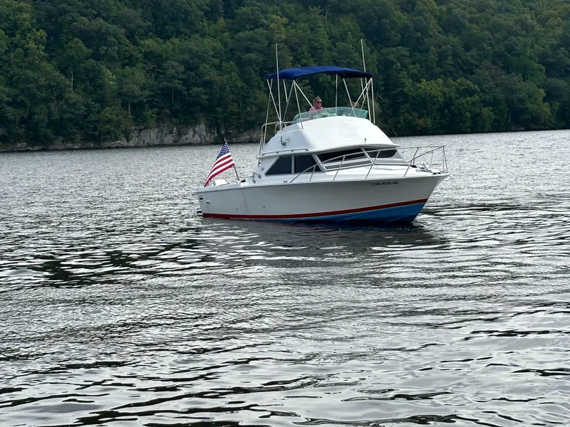 Slide: The Image of 1983 Bertram 28 boat cruising on a lake with forested shoreline. - 2
