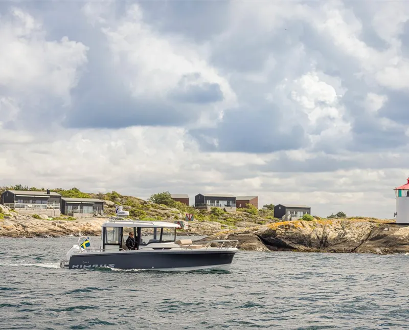 Slide: The Image of Nimbus C8 2024 boat cruising near rocky shoreline with lighthouse and houses in the background. - 21