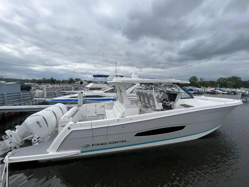 Slide: The Image of 2024 Regal 38SAV boat docked at a marina under cloudy skies. - 2