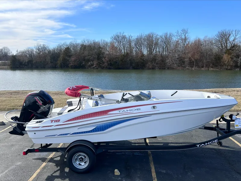 The Image of 2024 Tahoe T18 boat on trailer by a lake with trees in the background. - 0