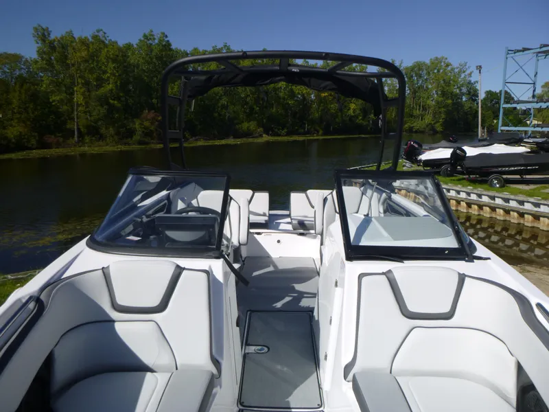 Slide: The Image of 2024 Yamaha Boats AR250 interior view with seating and windshield, docked by a serene lake. - 33