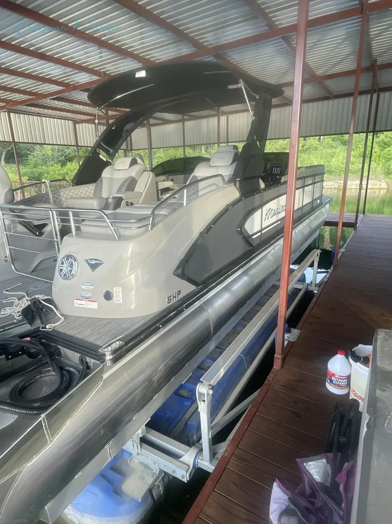 Slide: The Image of 2021 Manitou 27 LX SRW Duel Engine pontoon boat docked under a covered marina. - 10
