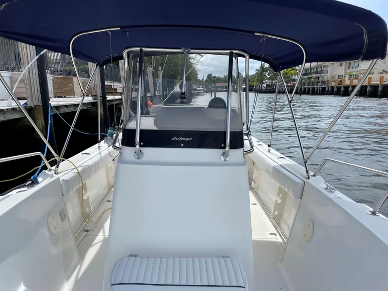 Slide: The Image of 1999 Boston Whaler Outrage 23 boat with blue canopy docked by the water. - 5