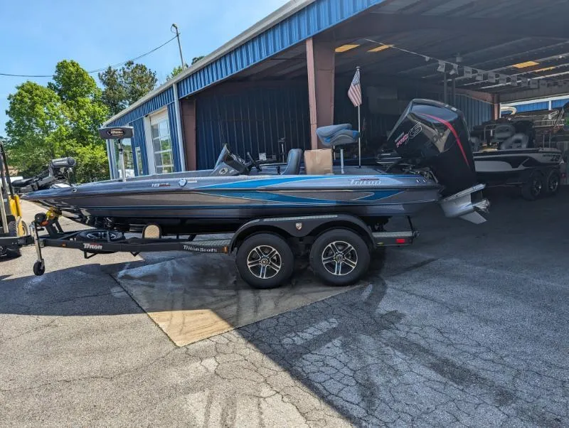 Slide: The Image of 2024 Triton 18 TrX bass boat on a trailer outside a blue building. - 7