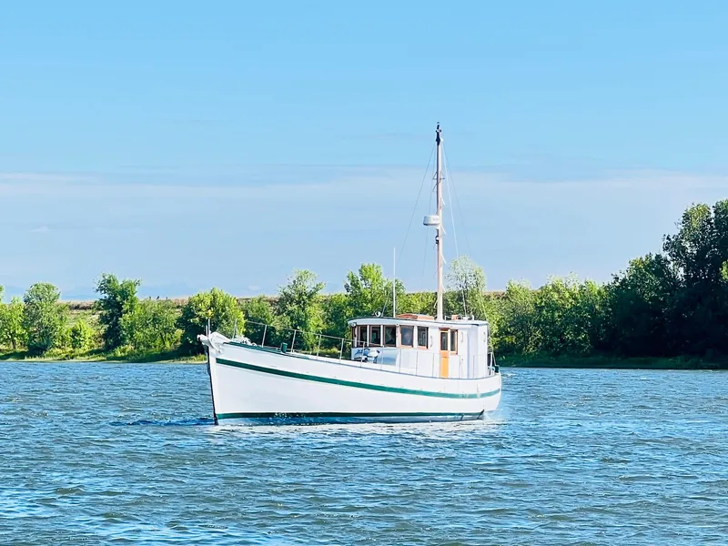 Slide: The Image of 1955 Colin Archer 42 boat sailing on a calm river with lush green trees in the background. - 3