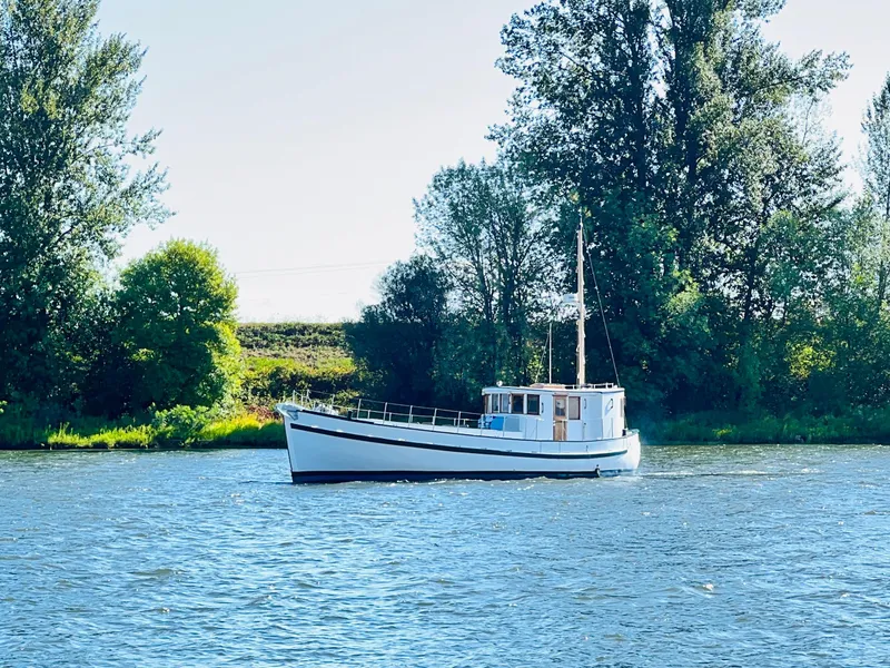 Slide: The Image of 1955 Colin Archer 42 boat on a serene river with lush green trees. - 40