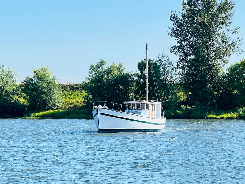 Slide: The Image of 1955 Colin Archer 42 boat sailing on a serene river with lush greenery. - 42