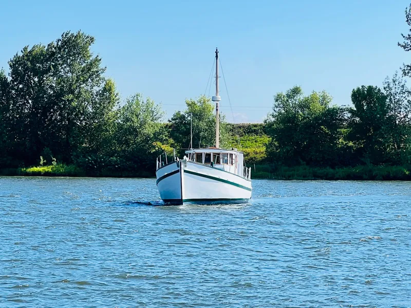 Slide: The Image of 1955 Colin Archer 42 boat cruising on a serene river with lush green trees in the background. - 44