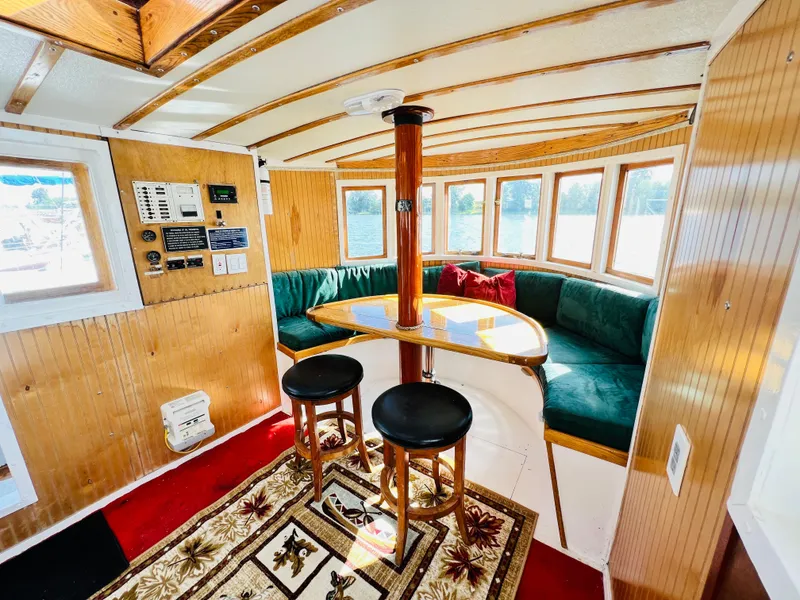 Slide: The Image of 1955 Colin Archer 42 boat interior with wooden paneling, round table, and green cushioned seating. - 9