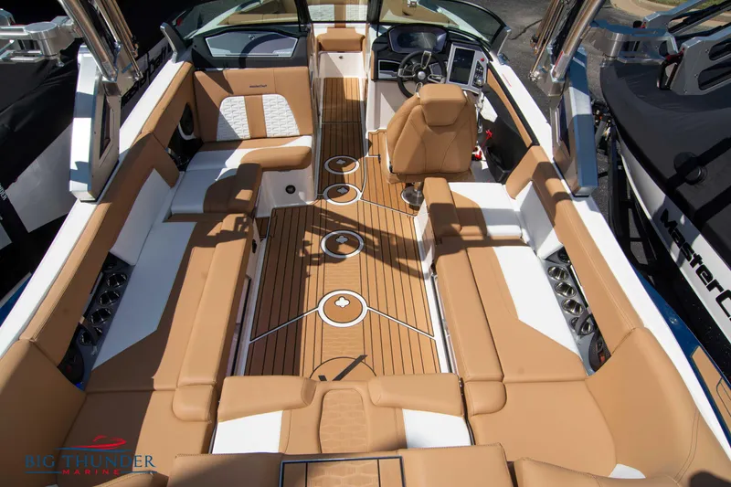 Slide: The Image of 2023 MasterCraft X24 boat interior with tan and white seating, teak flooring, and modern dashboard. - 14