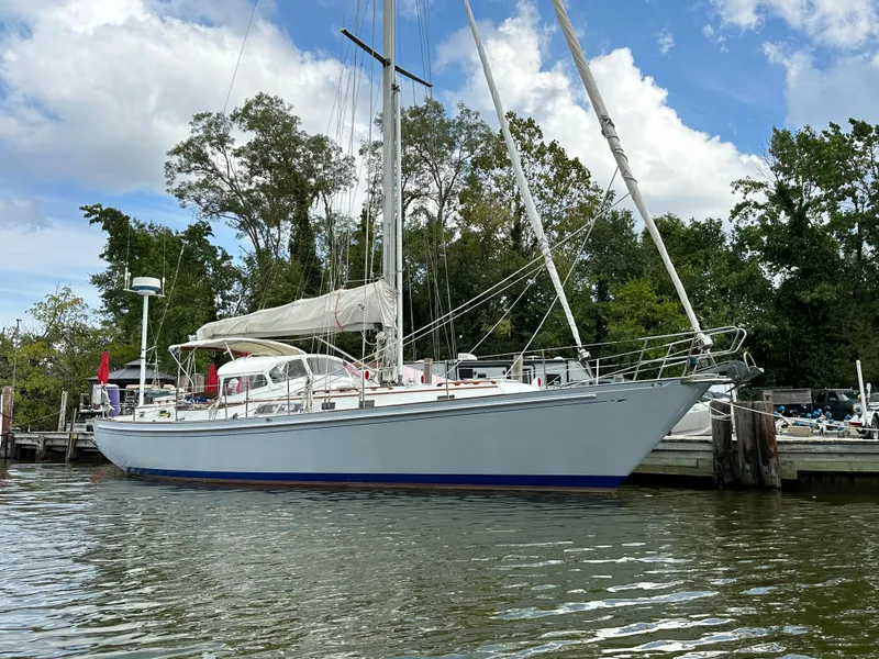 Slide: The Image of 1983 Brewer 42 Center Cockpit sailboat docked by a marina, surrounded by trees and calm water. - 0
