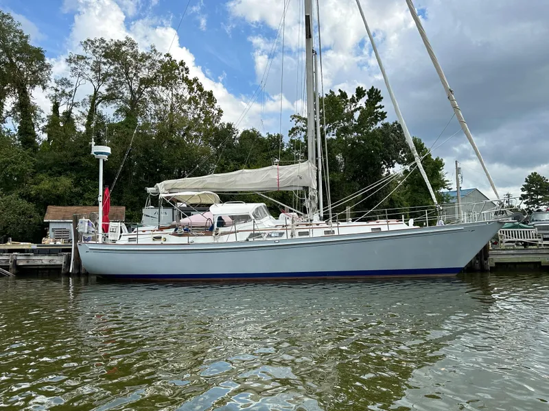 Slide: The Image of 1983 Brewer 42 Center Cockpit sailboat docked on a calm river under a cloudy sky. - 1