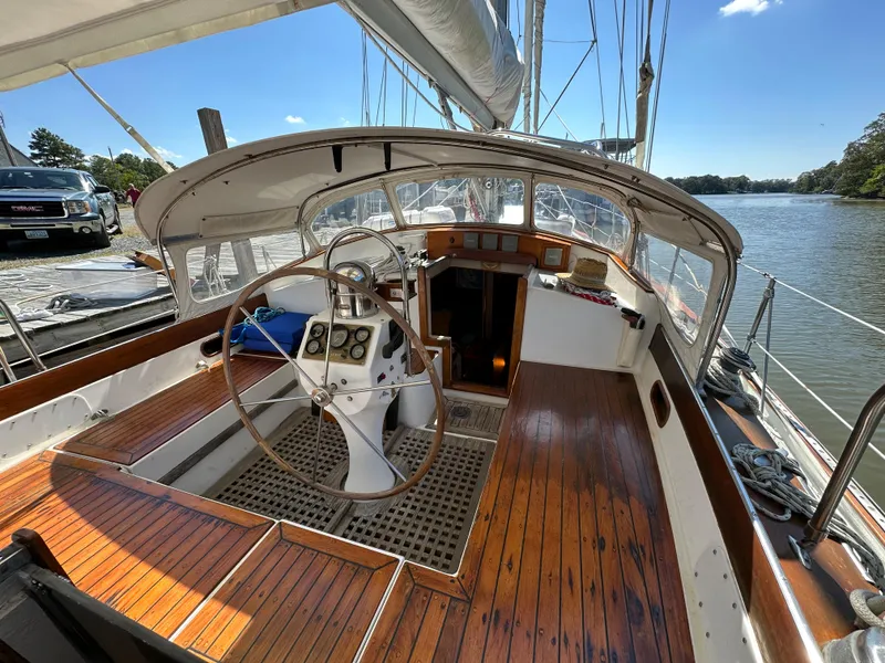 Slide: The Image of 1983 Brewer 42 Center Cockpit sailboat with wooden deck and steering wheel, docked by a river. - 30