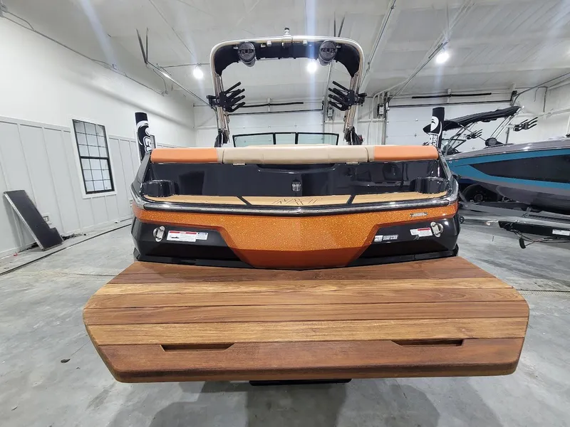 Slide: The Image of 2024 MasterCraft NXT22 boat in a showroom, rear view with wooden swim platform. - 11
