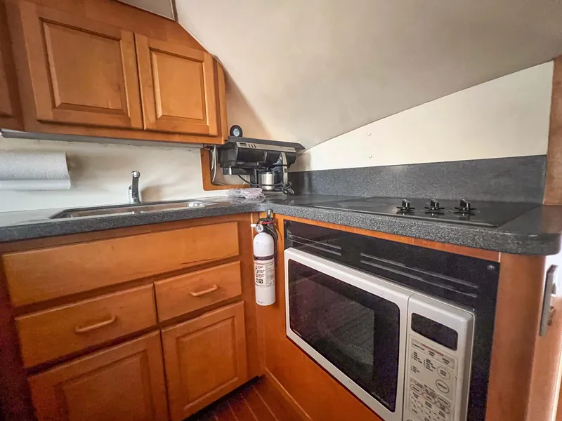 Slide: The Image of 2000 Luhrs 400 Convertible boat kitchen with wooden cabinets, stove, microwave, and sink. - 24