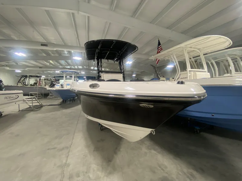 Slide: The Image of 2024 Robalo R202 Explorer boat in showroom, black hull, T-top, American flag. - 2