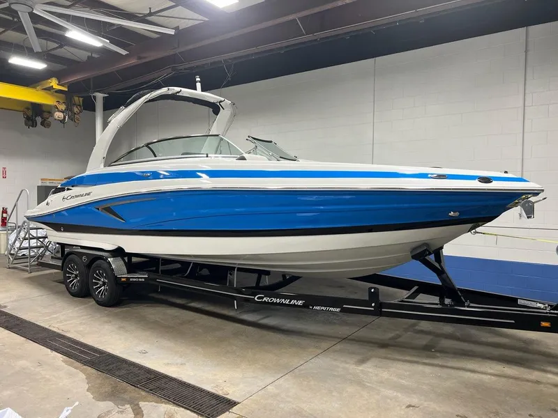 Slide: The Image of 2023 Crownline 290 SS boat in blue and white on a trailer in a warehouse. - 2