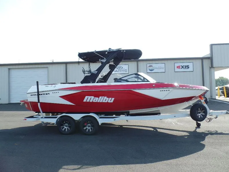Slide: The Image of 2024 Malibu 23 LSV boat in red and white on a trailer, parked outside a building. - 3