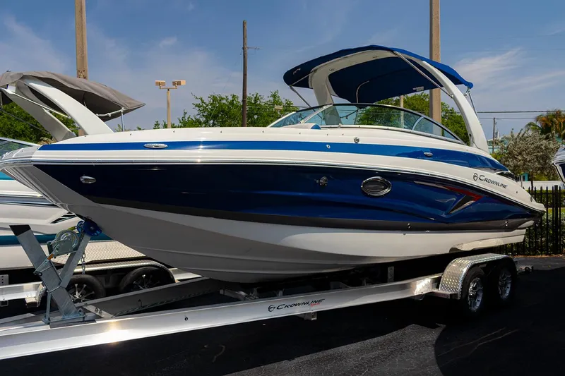 Slide: The Image of 2022 Crownline E 255 XS boat on a trailer, blue and white exterior. - 0