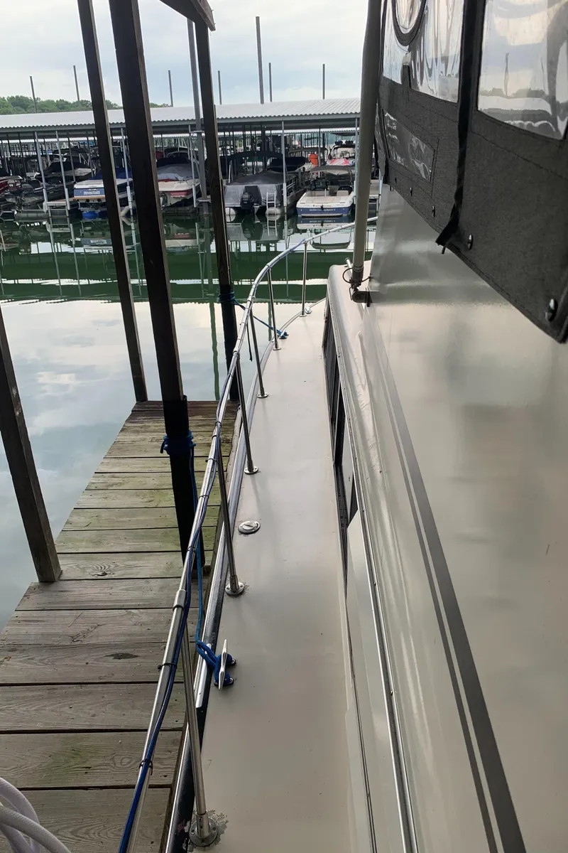 Slide: The Image of 1987 Marinette Fisherman boat docked at a marina, side view with railing and water reflection. - 4
