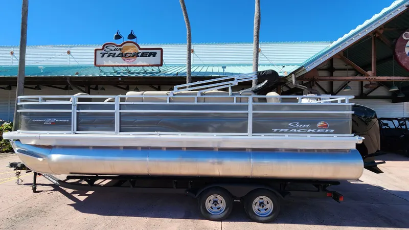 The Image of 2024 Sun Tracker Fishin' Barge 22 XP3 pontoon boat on trailer, dealership background. - 0