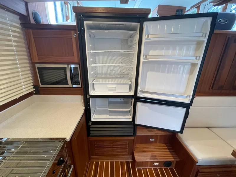 Slide: The Image of 2025 American Tug 362 galley with open refrigerator, microwave, and wooden cabinetry. - 21