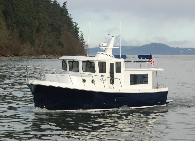 The Image of 2025 American Tug 365 cruising on calm waters near a forested shoreline. - 0
