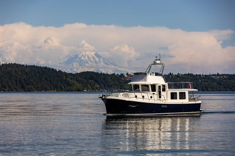 The Image of American Tug 395 (2026) cruising on a serene lake with mountain backdrop. - 0