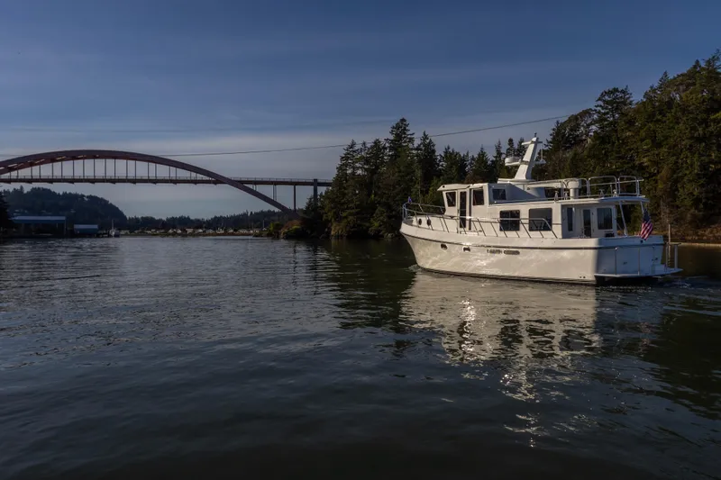 Slide: The Image of 2026 American Tug 435 cruising near a scenic bridge and forested shoreline. - 2