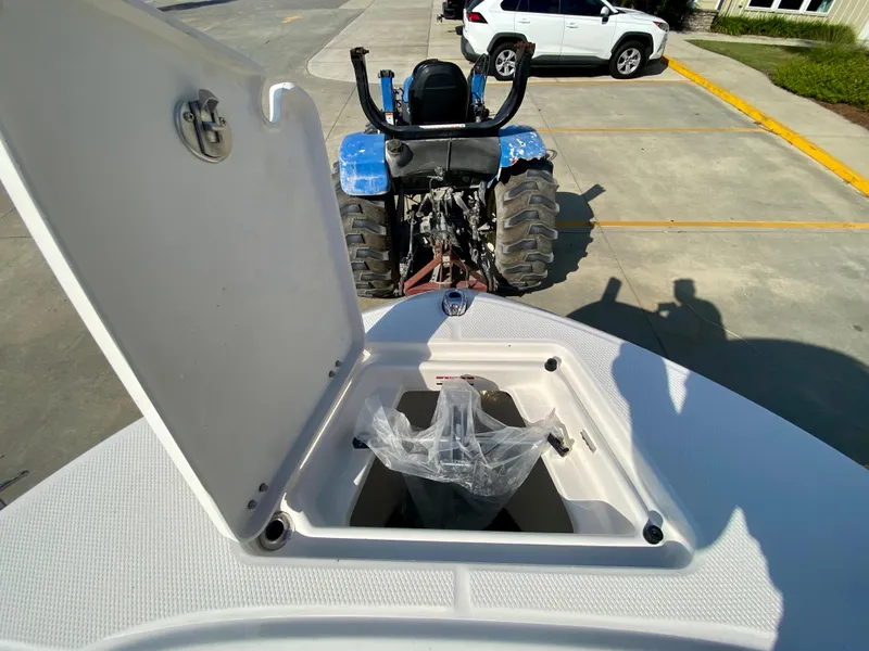 Slide: The Image of 2024 Robalo R180 Center Console boat with open storage compartment, parked near a tractor. - 19