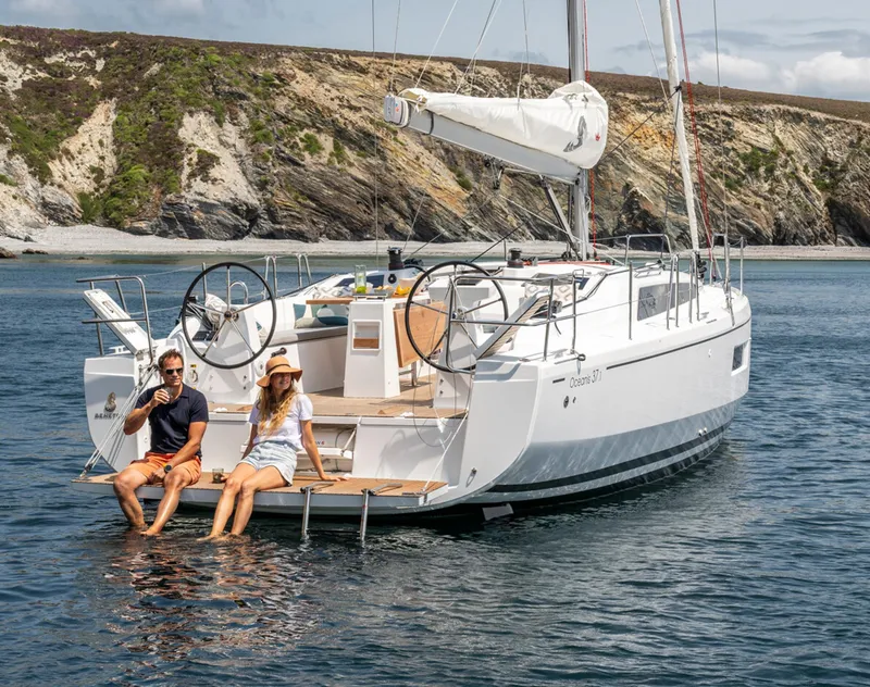 Slide: The Image of 2025 Beneteau Oceanis 37.1 sailboat with two people relaxing on deck in scenic waters. - 3