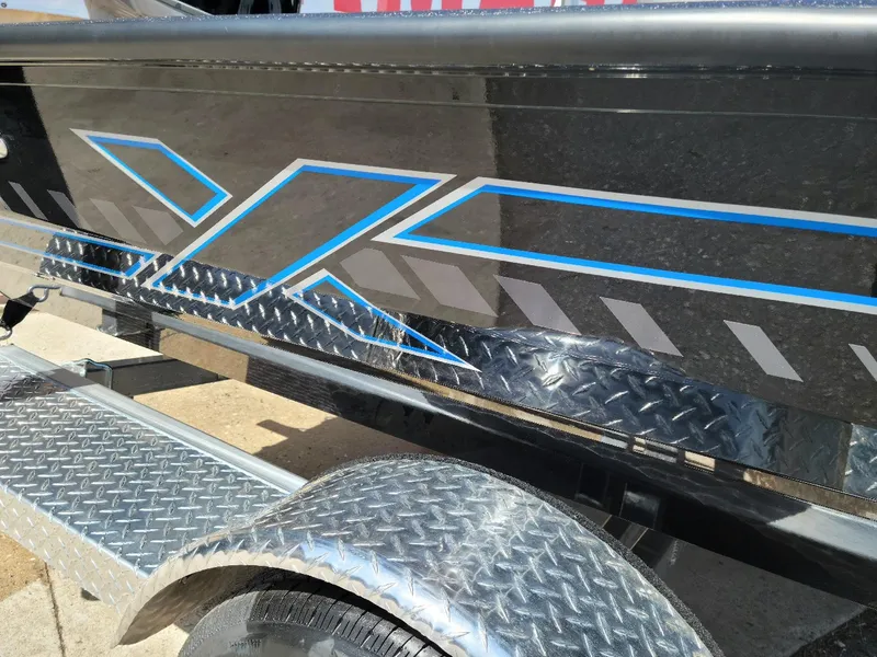 Slide: The Image of 2024 Xpress H18C Crappie Edition boat with blue and gray graphics on a diamond plate trailer. - 7