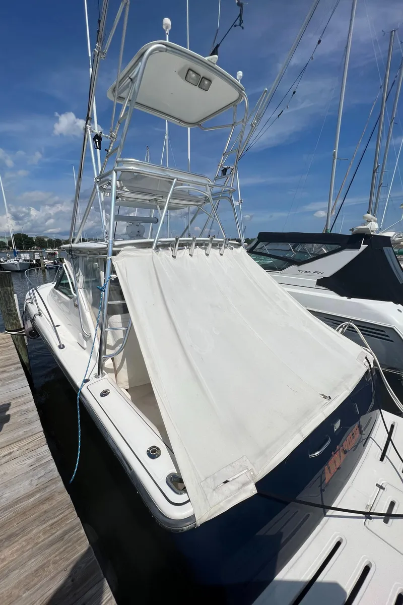 Slide: The Image of 2004 Tiara Yachts 3200 Open docked, featuring a white canopy and upper deck. - 3