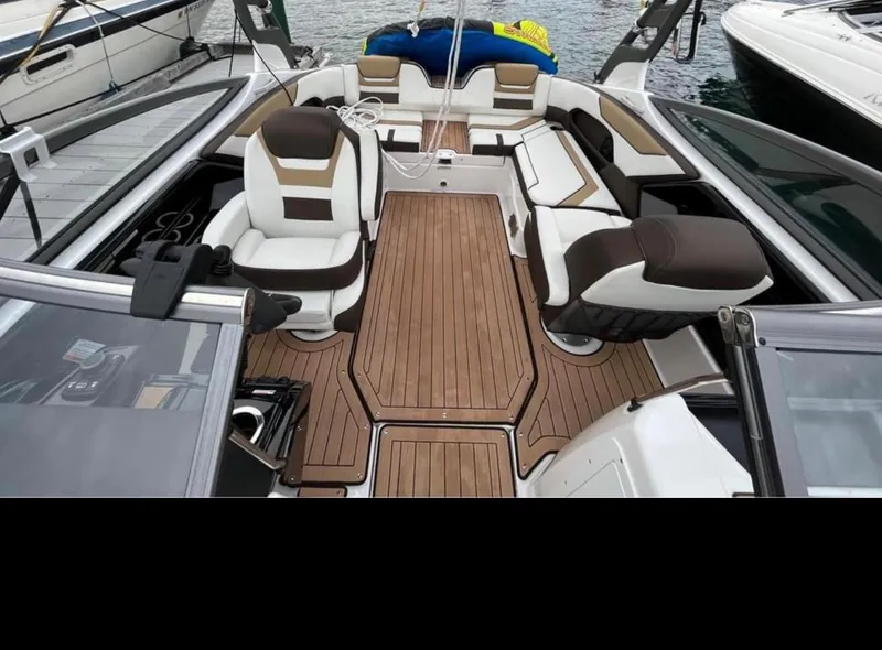 Slide: The Image of 2021 Yamaha Boats 212S interior with brown and white seating, wooden flooring, docked. - 3