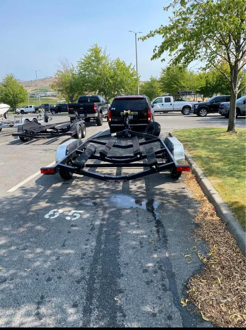 Slide: The Image of 2021 Yamaha Boats 212S trailer parked in a lot with trees and vehicles. - 7