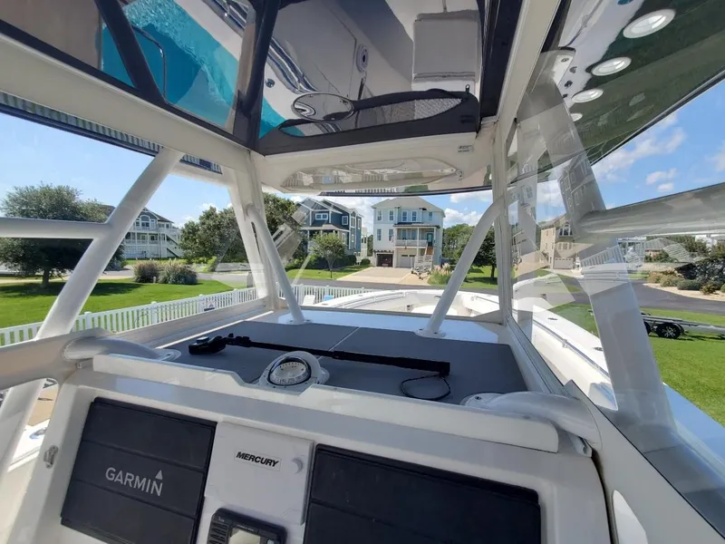 Slide: The Image of 2019 Invincible 39 CC boat cockpit with Garmin and Mercury controls, docked near waterfront homes. - 23