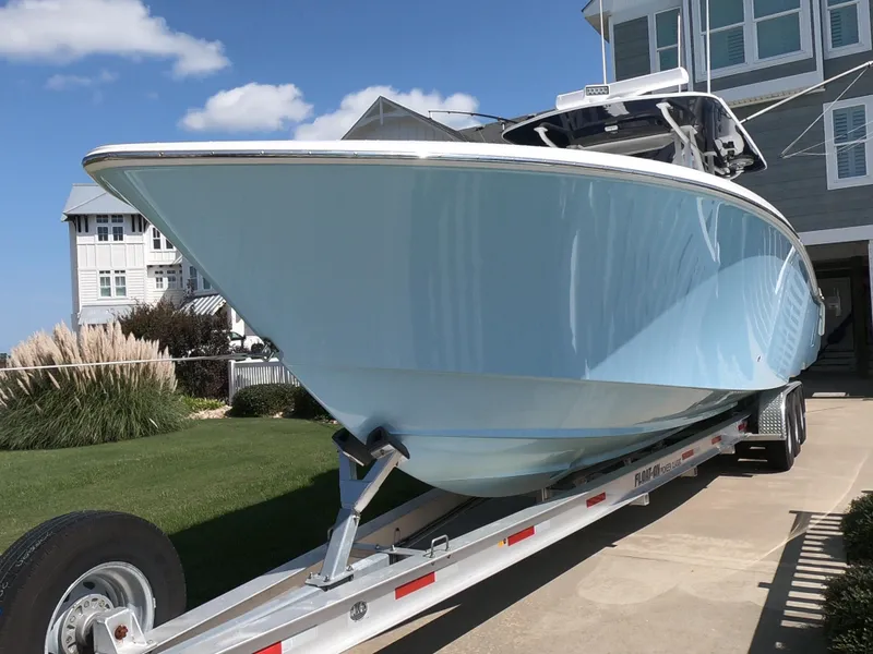 Slide: The Image of 2019 Invincible 39 CC boat on trailer, parked near coastal house under blue sky. - 3