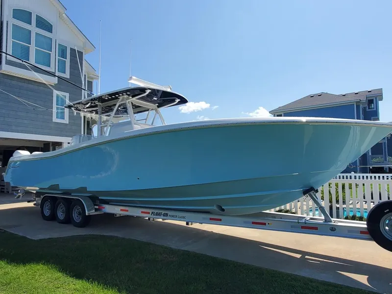 Slide: The Image of 2019 Invincible 39 CC boat on trailer, parked near coastal homes under clear blue sky. - 32