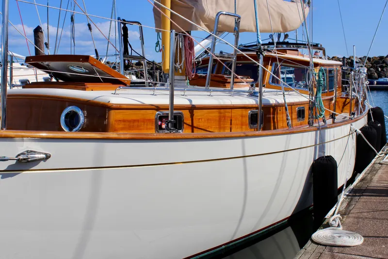 Slide: The Image of 2018 Cape George 45 sailboat docked, featuring classic wooden design and sleek white hull. - 5
