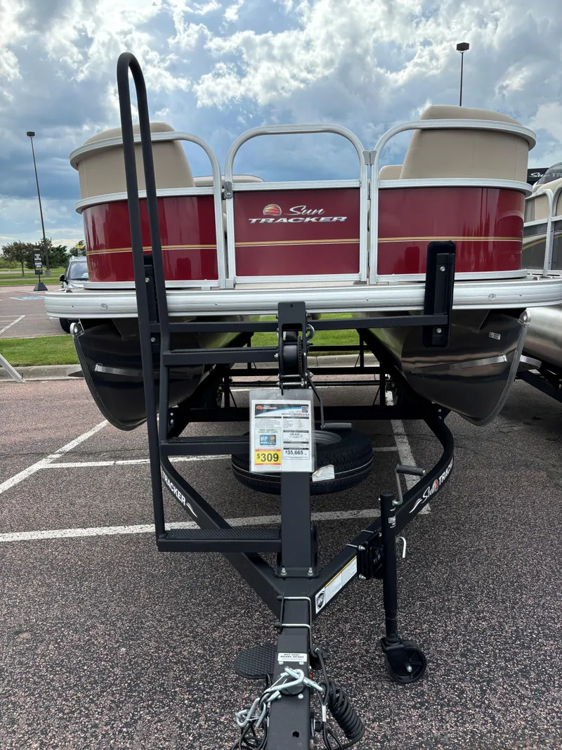 Slide: The Image of 2024 Sun Tracker Party Barge 18 DLX pontoon boat on a trailer in a parking lot. - 2