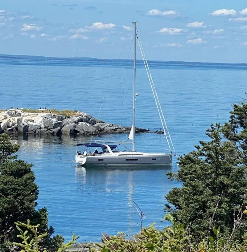 The Image of 2019 Beneteau 51.1 sailboat anchored near rocky shoreline, surrounded by calm blue waters. - 0