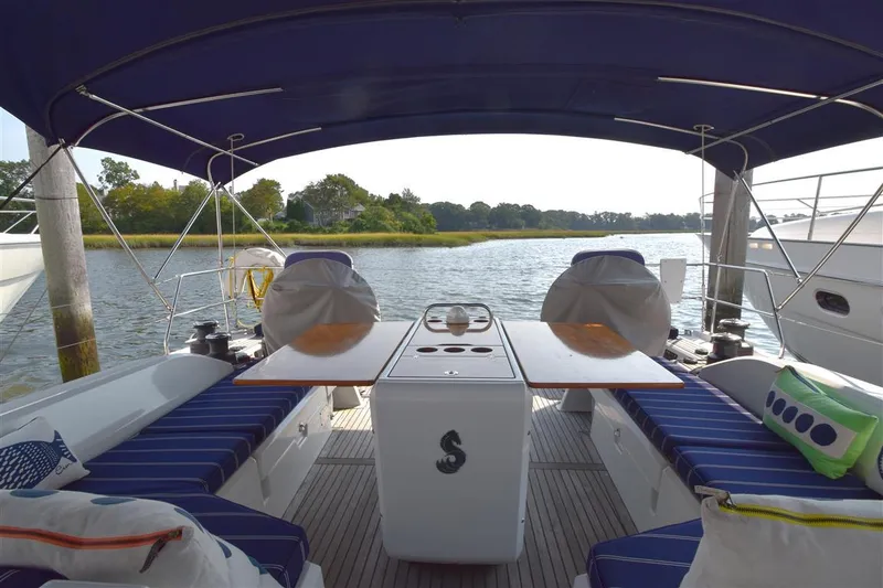 Slide: The Image of 2019 Beneteau 51.1 yacht cockpit with blue seating and table, docked by serene water. - 25