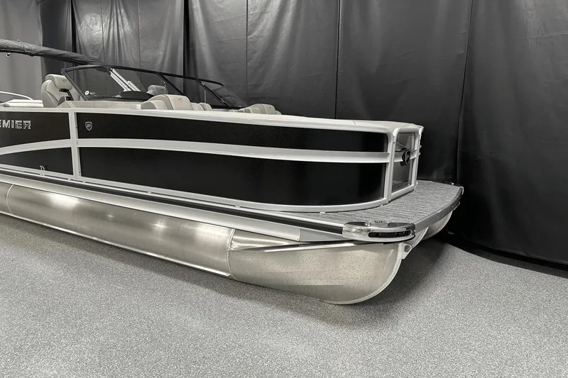Slide: The Image of 2024 Premier 250 Solaris Sport pontoon boat in showroom with sleek black and silver design. - 2
