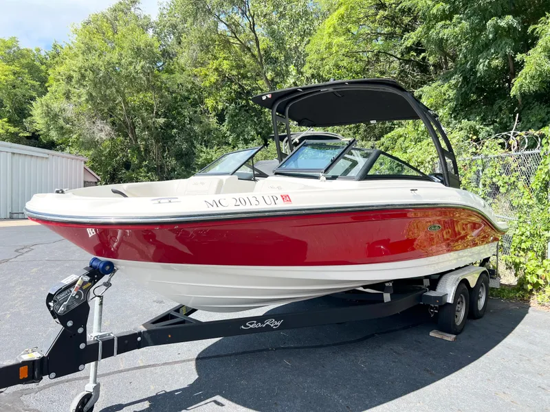 Slide: The Image of 2021 Sea Ray SPO 210 boat with red hull on trailer, parked outdoors. - 2