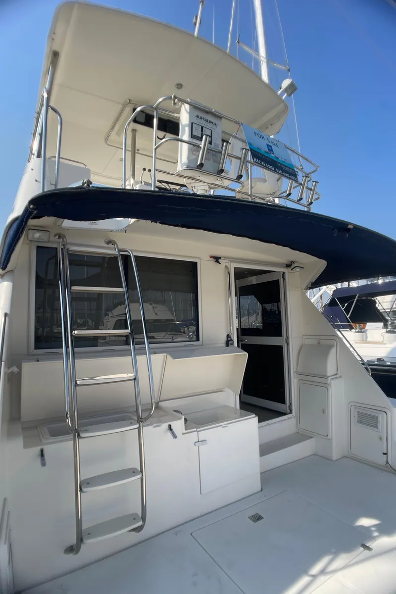 Slide: The Image of 2000 Riviera Flybridge yacht with ladder and upper deck, docked under clear blue sky. - 26