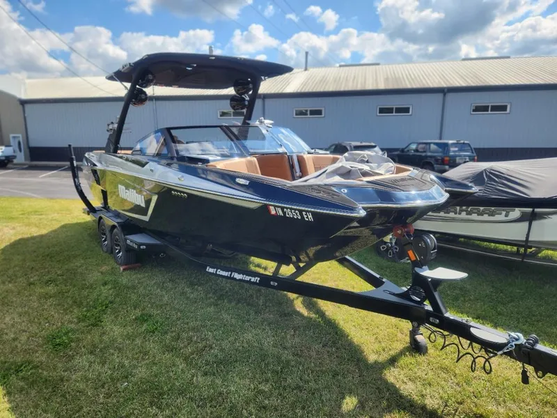 Slide: The Image of 2021 Malibu Wakesetter 24 MXZ boat on trailer, parked on grass under a cloudy sky. - 0