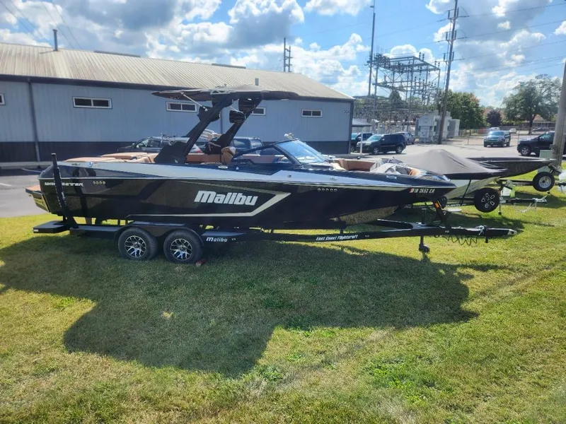 Slide: The Image of 2021 Malibu Wakesetter 24 MXZ boat on trailer, parked on grass under a cloudy sky. - 1