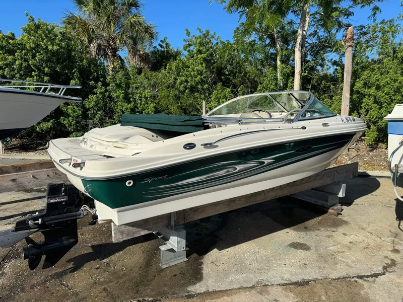 Slide: The Image of 2005 Sea Ray 180 Sport boat on a lift, surrounded by trees and other boats. - 30