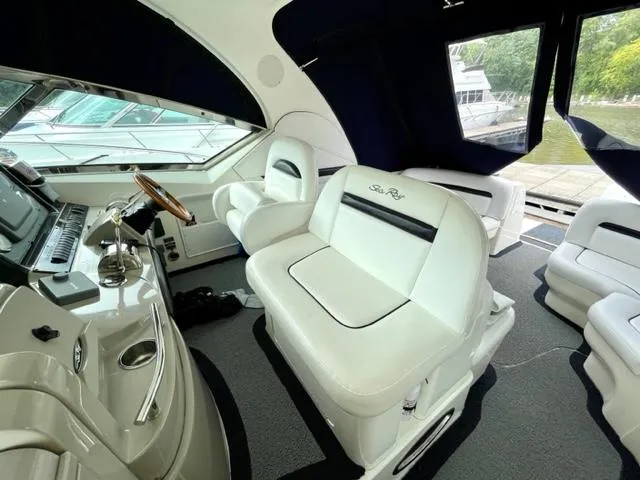 Slide: The Image of 2007 Sea Ray 38 Sundancer interior with white seating and helm, docked by the water. - 9