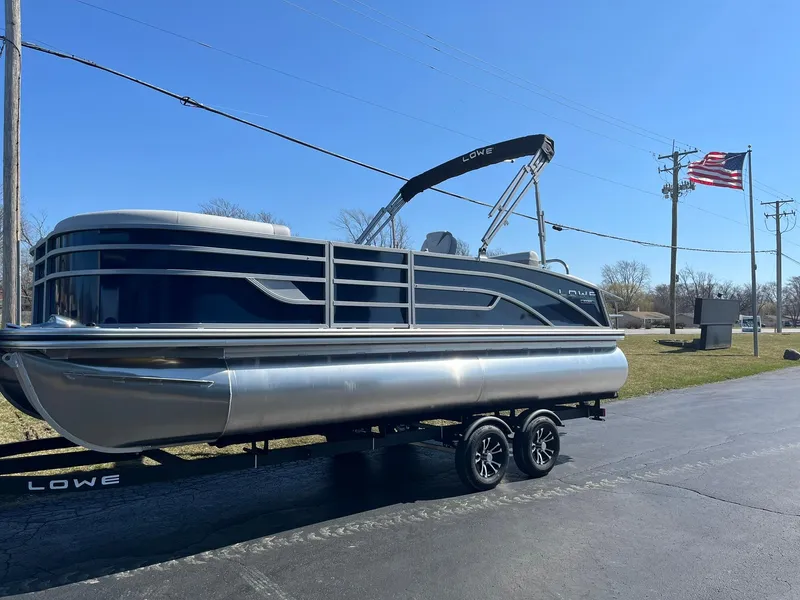 Slide: The Image of 2024 Lowe SS 210 DL pontoon boat on a trailer with an American flag in the background. - 2